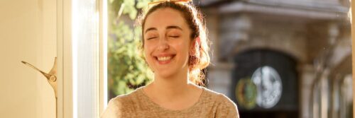 A woman in her forties smiling calmly by a sunlit window, showing life after recovering from chronic stress effects