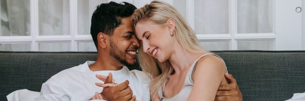 A couple smiling cheek to cheek on a sofa, secure and at ease together