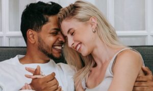 A couple smiling cheek to cheek on a sofa, secure and at ease together