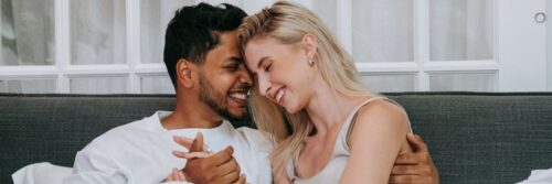 A couple smiling cheek to cheek on a sofa, secure and at ease together