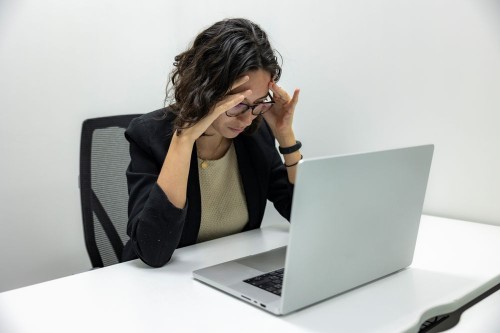 An employee holding her head in her hands at her laptop, overwhelmed at work