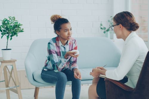 One woman listening warmly to another across a table in a bright modern room, showing the support that helps ease rejection sensitivity