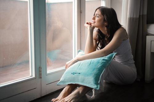 A woman sitting alone by a tall window holding a cushion while she waits, reflecting the restlessness of fear of abandonment