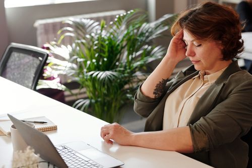An employee staring at a laptop late in the day looking drained, a common sign of unmanaged psychosocial hazards at work