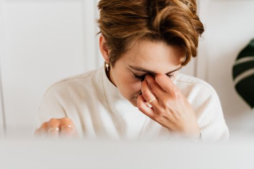 A tired woman rubbing her neck at a table in warm afternoon light, showing the physical chronic stress effects that build over months