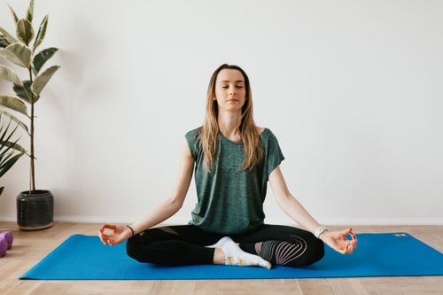 A woman sitting upright in a bright room with her eyes closed, practising slow breathing as a first step in nervous system regulation