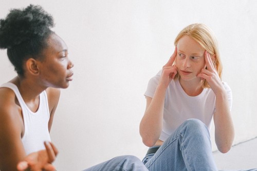 A woman pressing her temples while a friend unloads, absorbing the collective energy of the conversation