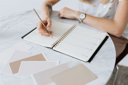 A woman writing in a weekly planner at a sunlit table, planning ahead to reduce decision fatigue