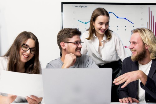 A team laughing together around a laptop in a bright office, sharing positive collective energy at work