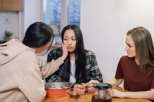 A friend reaching out to a quiet woman at the table, the first step away from feeling invisible