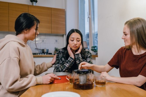 A woman sitting quietly at a kitchen table while her friends talk across her, feeling invisible