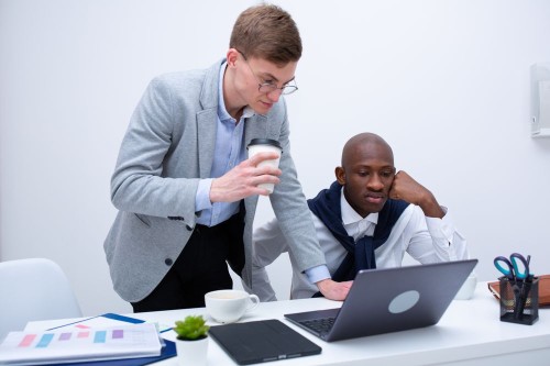A colleague holding a coffee talks down to a coworker at his desk, an everyday example of workplace incivility