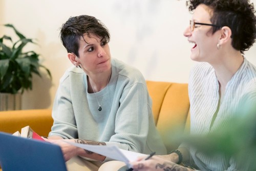 Two friends in a warm, easy conversation on a yellow sofa, steadying each other's energy