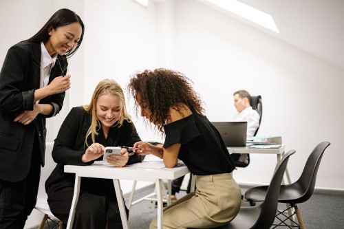 Three colleagues sharing a laugh over a phone in a bright office, a team where respect is the norm