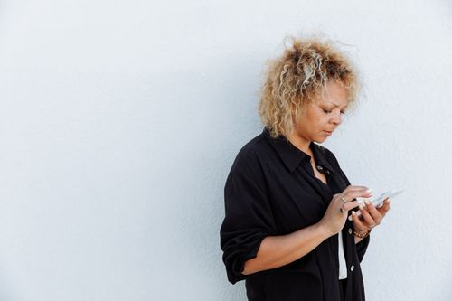 A woman in her forties looking anxiously at her phone by a sunlit window, showing how rejection sensitivity reads a short reply as a slight