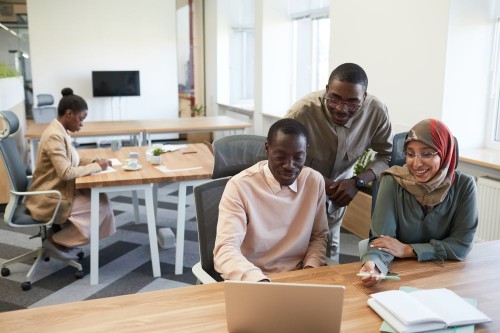 A relaxed team smiling together around a laptop in a bright, modern office