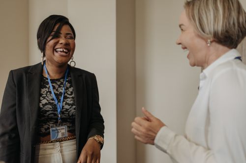 Two colleagues laughing easily at a desk in a bright office, showing a team recovering from workplace incivility