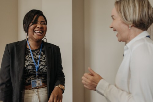Two colleagues laughing together in an easy one to one conversation, the trust trauma informed leadership builds