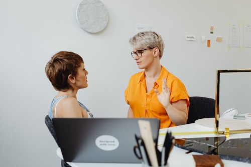 Two colleagues in an attentive one-to-one conversation at a desk, the kind of listening trauma-informed leadership depends on