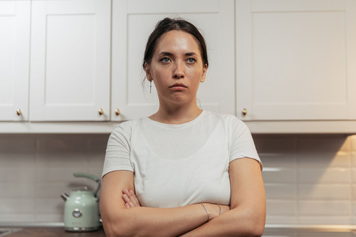 A woman standing tense and preoccupied in a bright kitchen in the morning, showing how emotional resonance carries into the day
