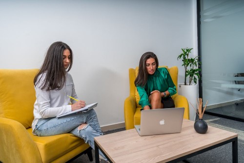 A manager and employee in a calm one-to-one conversation on yellow armchairs in a bright office