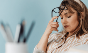 Decision fatigue as a woman in a striped shirt sits at her desk with her glasses on her head as she tries to make a decision