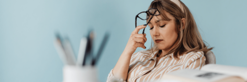 Decision fatigue as a woman in a striped shirt sits at her desk with her glasses on her head as she tries to make a decision
