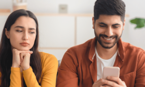 Trust issues in relationships between a woman with dark hair in a yellow top and a man in a brown shirt looking at his phone
