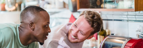 Two friends in their forties talking and laughing over breakfast in a bright modern kitchen, showing the calm start that morning energy rituals create