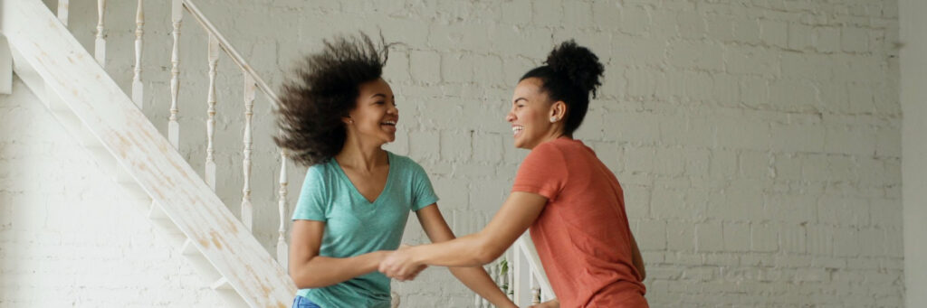 Two friends in their forties laughing together in a bright modern kitchen, showing what it looks like when low energy emotions have lifted
