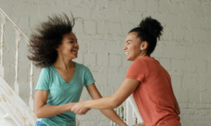 Two friends in their forties laughing together in a bright modern kitchen, showing what it looks like when low energy emotions have lifted