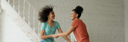 Two friends in their forties laughing together in a bright modern kitchen, showing what it looks like when low energy emotions have lifted