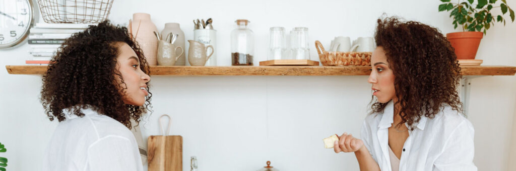 Two women in their forties talking easily over coffee in a bright modern kitchen, showing what self-worth and boundaries look like in practice