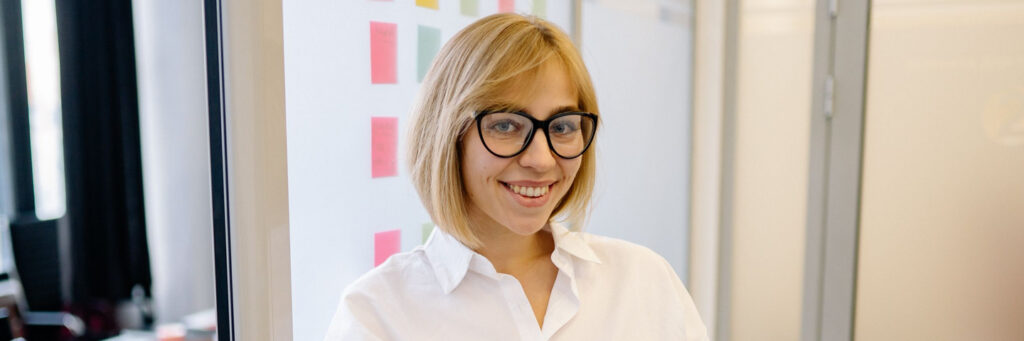 A woman in her forties smiling confidently at her desk in a bright modern office, showing life beyond imposter syndrome