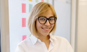 A woman in her forties smiling confidently at her desk in a bright modern office, showing life beyond imposter syndrome