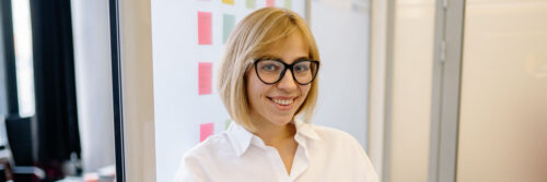 A woman in her forties smiling confidently at her desk in a bright modern office, showing life beyond imposter syndrome