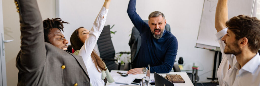 A manager and two colleagues laughing together around a table in a bright modern office, showing what happens after learning how to review workload at work