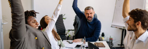 A manager and two colleagues laughing together around a table in a bright modern office, showing what happens after learning how to review workload at work