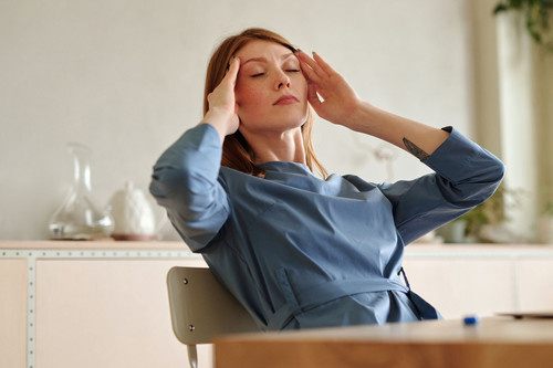 A tired woman in her forties sitting at a bright kitchen table looking drained, showing common chronic stress symptoms