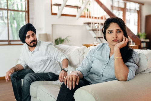 A couple sitting apart in silence in a bright living room, showing how resentment in relationships often looks from the outside