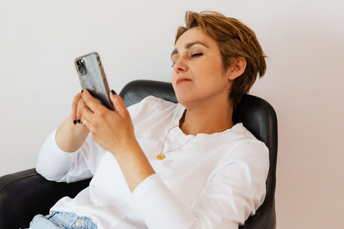 A woman sitting with her phone looking deflated in a bright modern room, the moment comparing yourself to others takes hold