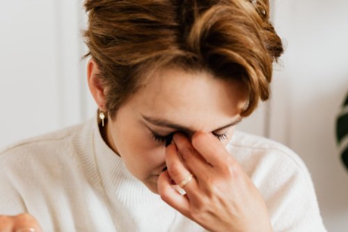 A tired woman rubbing her neck at a table in warm afternoon light, showing the physical chronic stress effects that build over months
