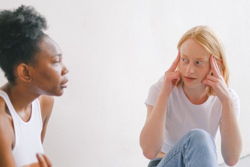 A woman pressing her temples while a friend unloads, absorbing the collective energy of the conversation