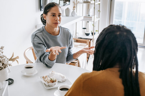 One woman listening closely to another in a bright daylit room, the point where fear of rejection begins to ease