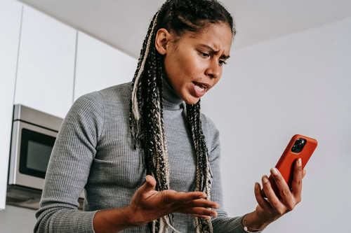A woman looking anxiously at her phone in a bright modern living room, showing how jealousy in relationships often begins