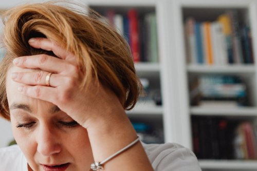 A woman looking stretched and overwhelmed at a bright kitchen table, the exhaustion that comes with people pleasing