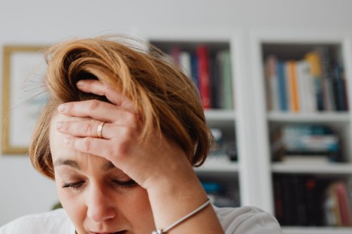 A woman looking stretched and overwhelmed at a bright kitchen table, the exhaustion that comes with people pleasing