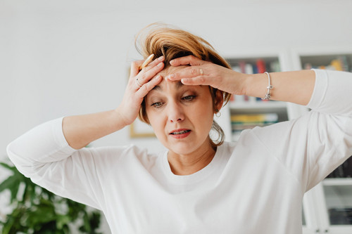 A woman looking drained as she checks her phone in a bright kitchen, showing how weak self-worth and boundaries lead to over-giving