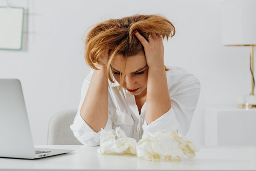 A woman in her forties looking overwhelmed at her desk in a bright office, the problem that prompts managers to learn how to review workload at work