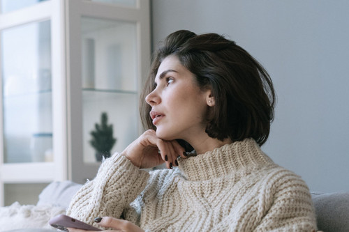 A woman in her forties sitting quietly by a window in a bright room, showing the heaviness people face when working out how to deal with grief and loss